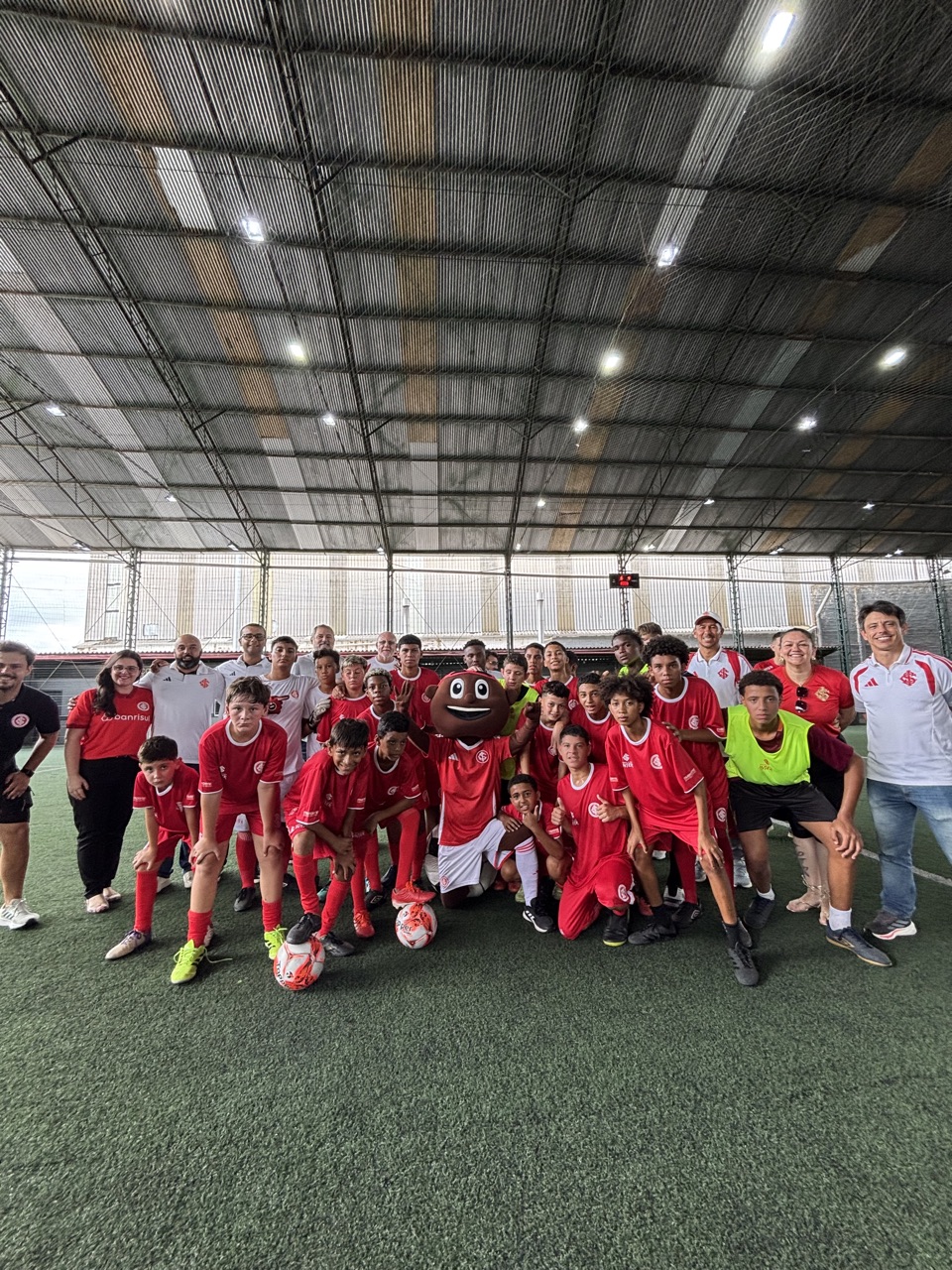 Turma da Escola do Inter reunida em campo, com uniforme vermelho e o mascote do Colorado